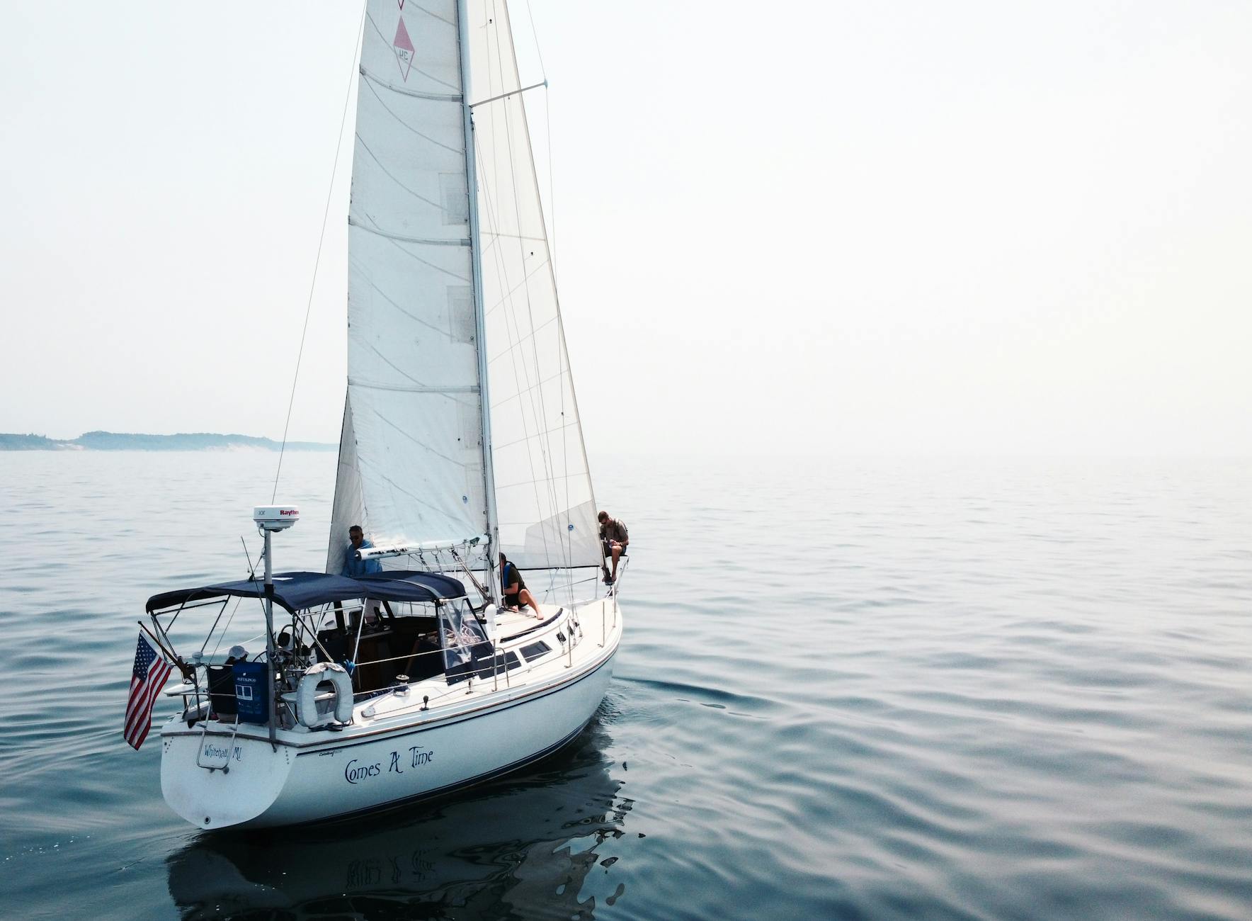 Jacht żaglowy płynie po spokojnym jeziorze przy bezchmurnym niebie