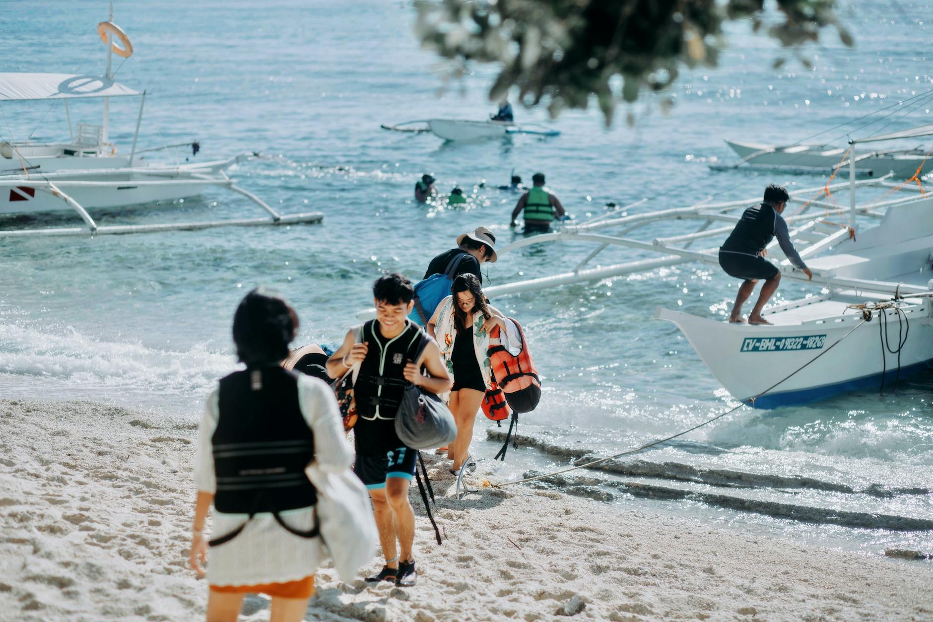 Turyści na piaszczystej plaży zakładają kamizelki przed rejsem łodzią