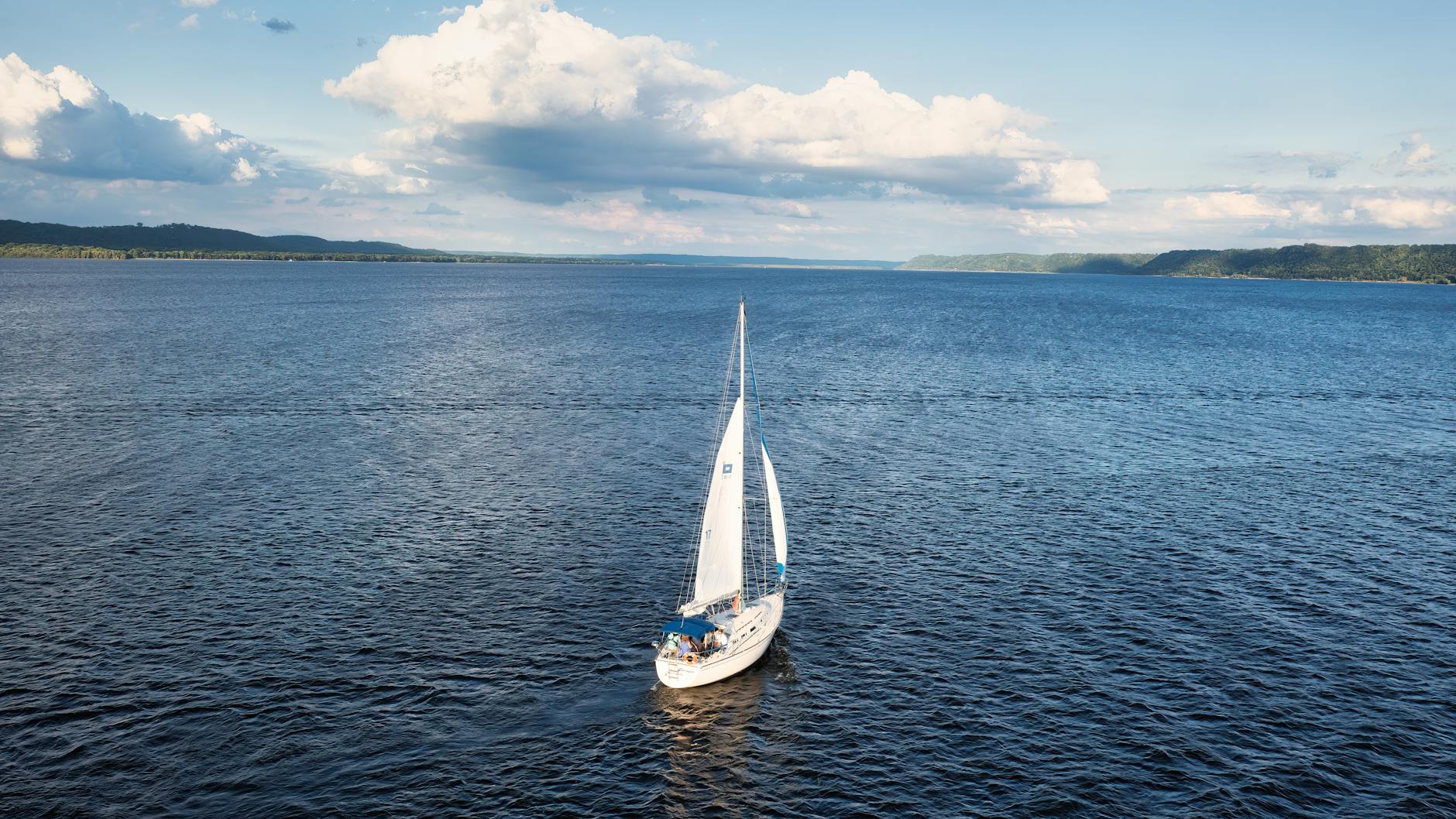 Żaglówka płynie po spokojnej tafli jeziora o zmierzchu