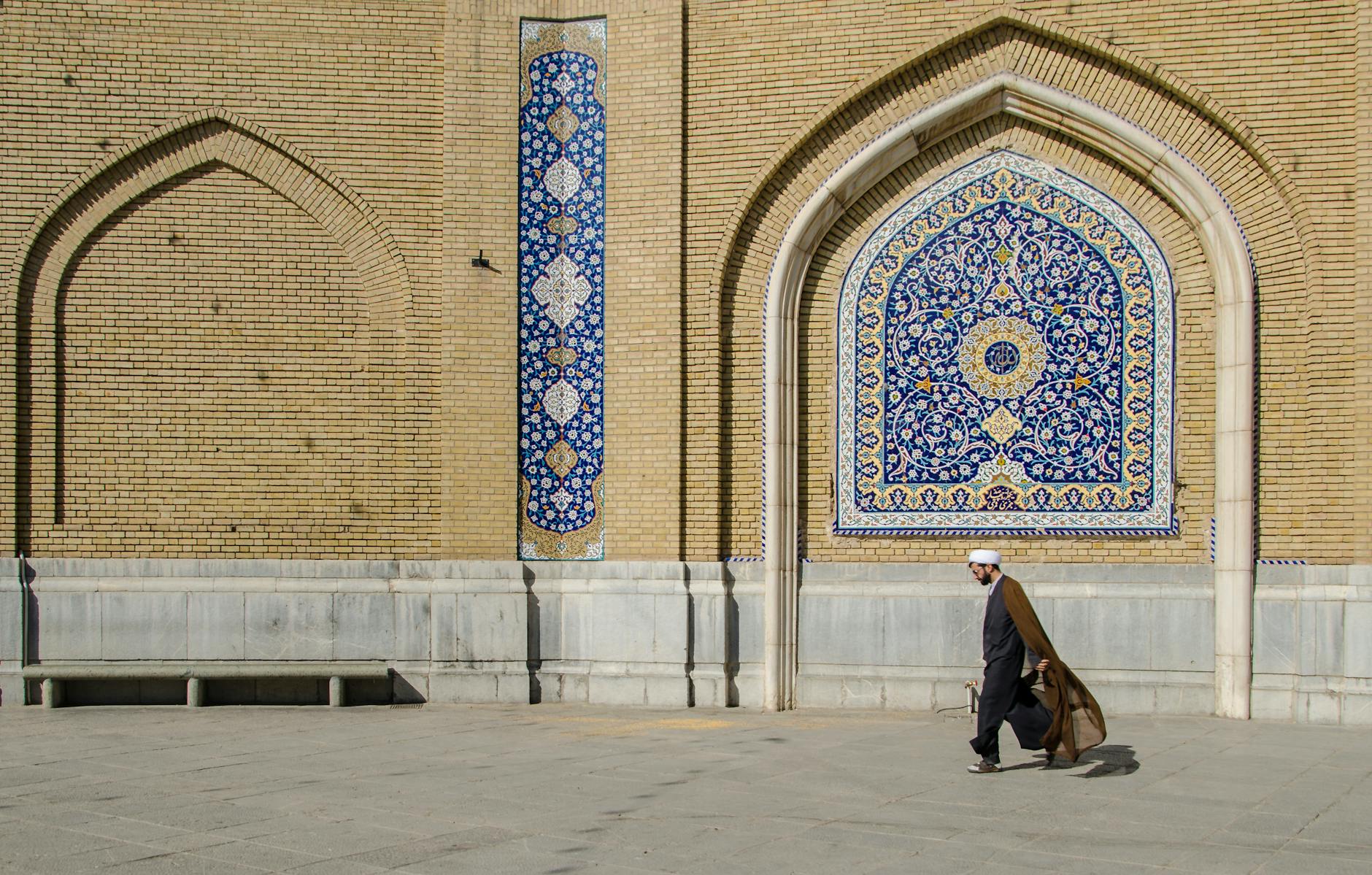 Mężczyzna idący obok bogato zdobionej ściany meczetu w Qom, Iran
