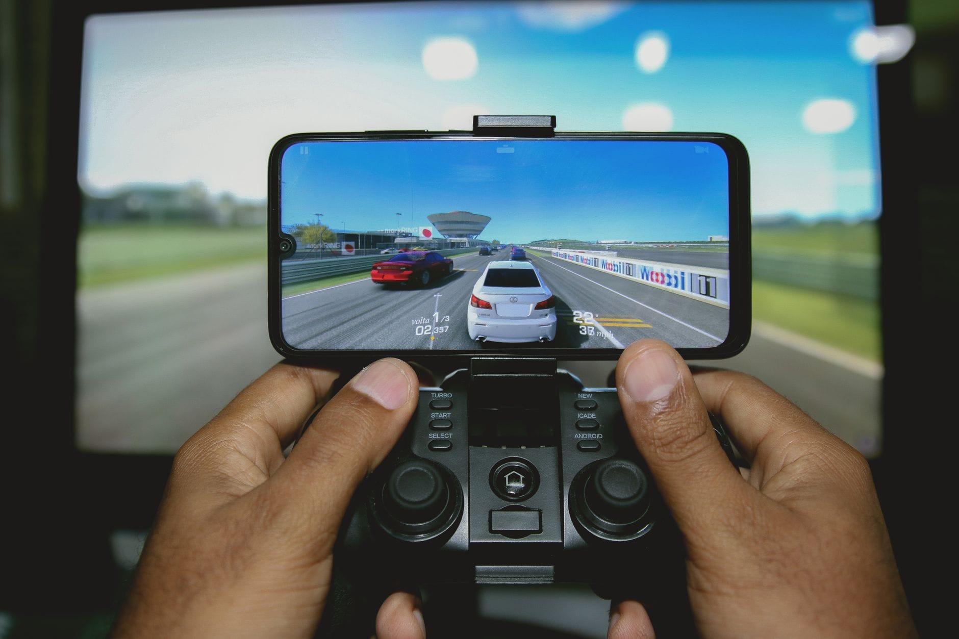 Dłonie grające w wyścigową grę MMO na smartfonie z kontrolerem