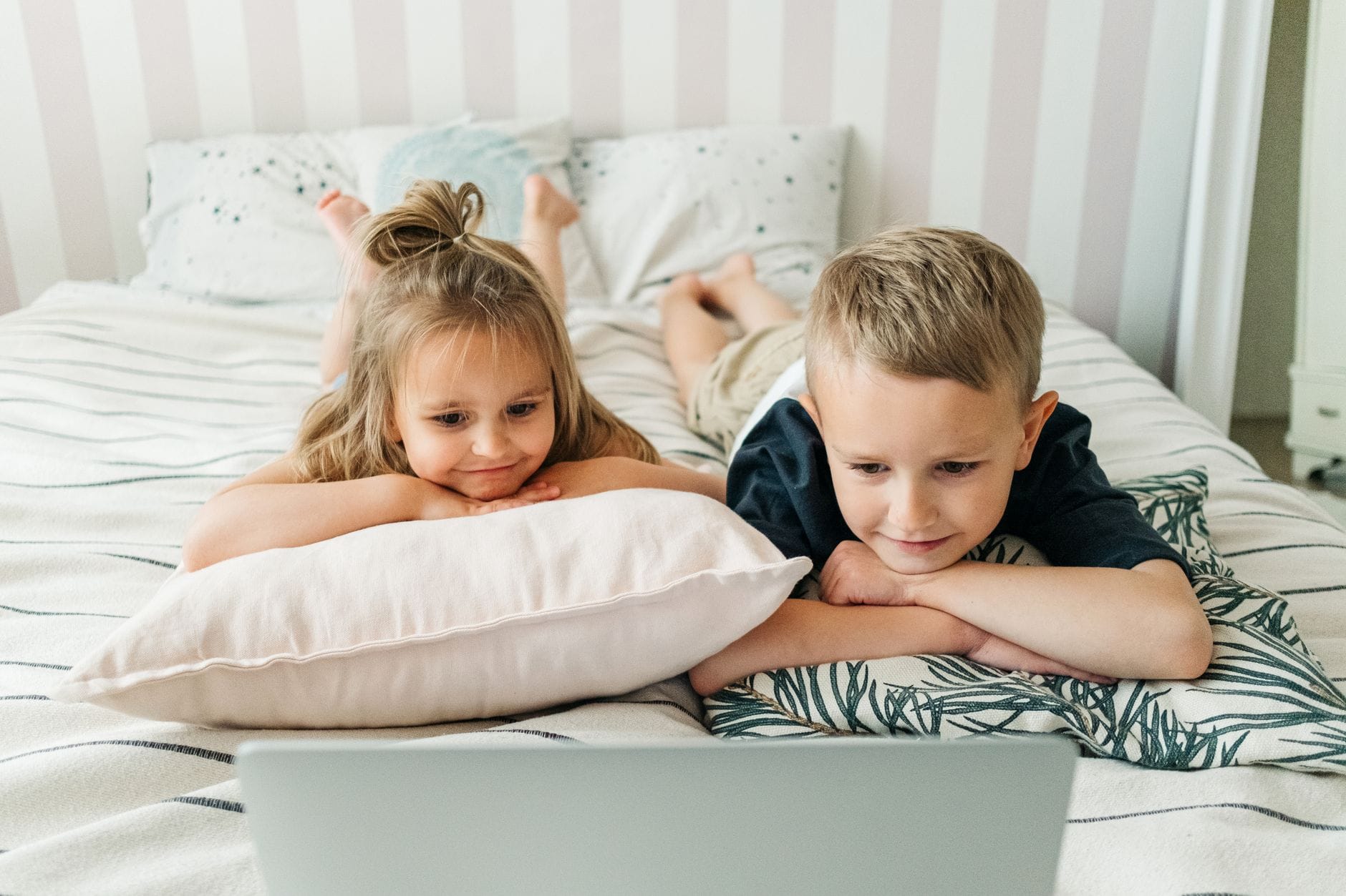 Dwoje dzieci na łóżku ogląda laptop w przytulnym wspólnym pokoju