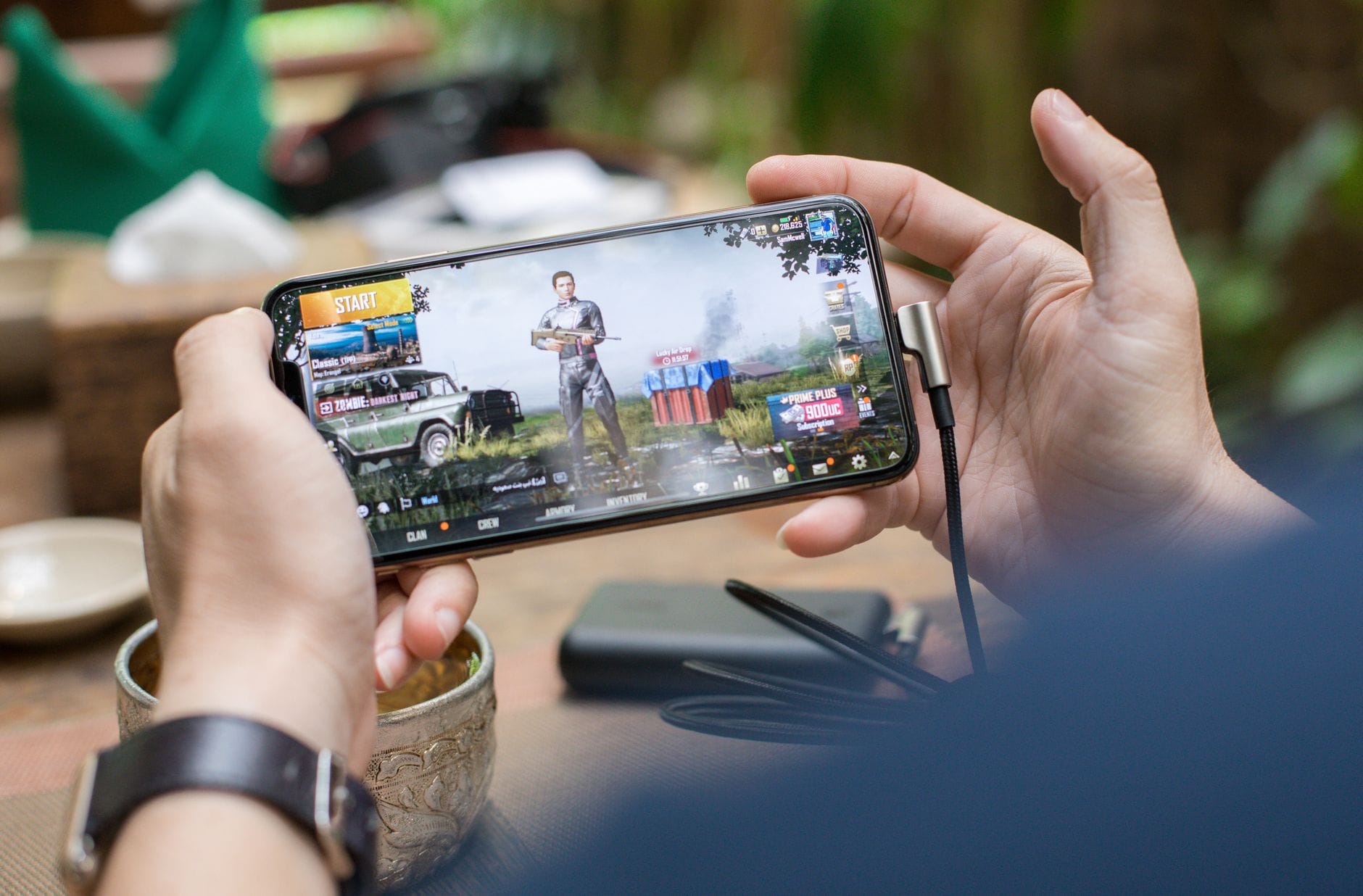 Osoba grająca w PUBG na smartfonie na dworze z podłączoną ładowarką